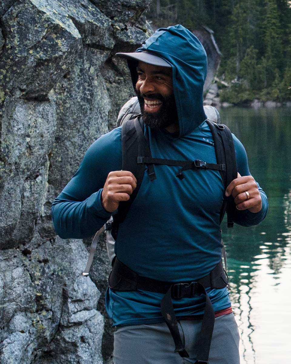 Man smiling while hiking with a pack on. He is wearing the Men's Geo-T in steel blue. Men's Geo-T Crew L.S. Shirt - Beyond Clothing USA