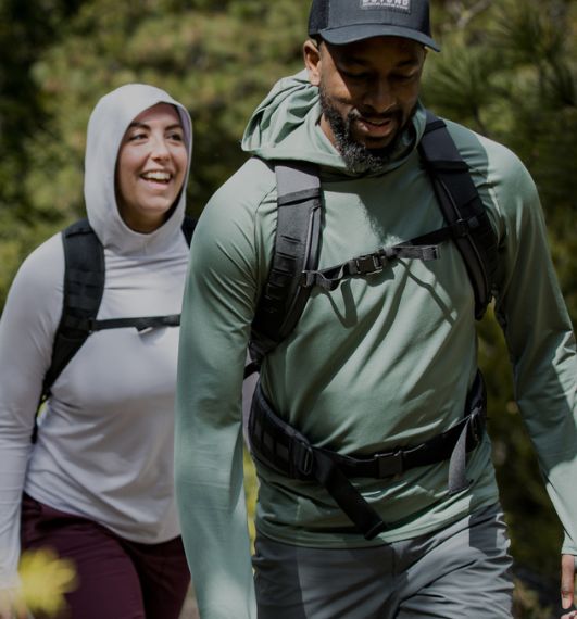 Man wearing Dark Mint Geo-T Hooded L.S. Shirt and Woman wearing Lilac Grey Hooded L.S. Shirt hiking up a trail