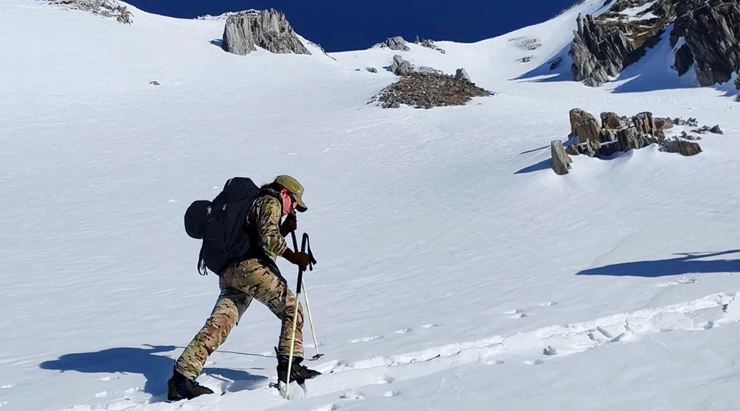 Woman skiing up a snowy mountain with backpack and skis.