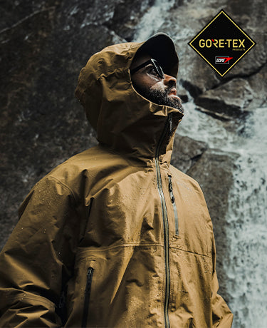 Hiker wearing the Drilight Jacket from Beyond near a water fall. GORE-TEX Fabrics logo shown.