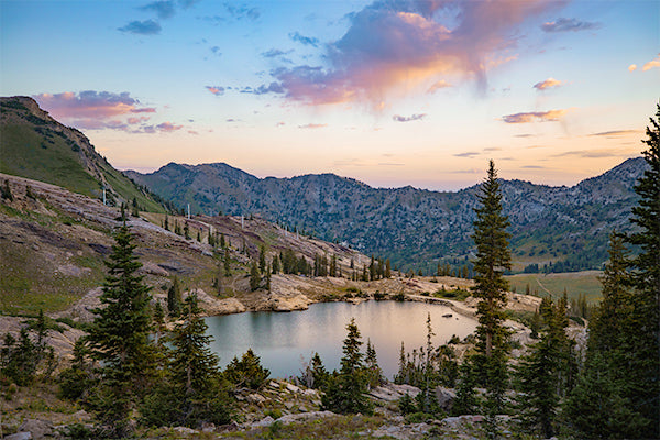 Mountain lake at sunset with trees and rocks around the shores. 