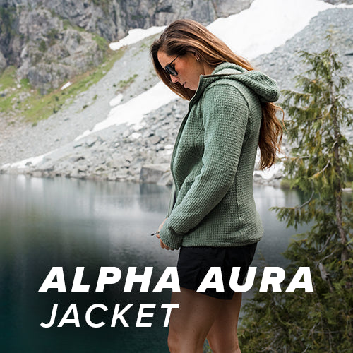 Hiker wearing the Beyond Clothing Alpha Aura Jacket in the mountain range next to a lake. 