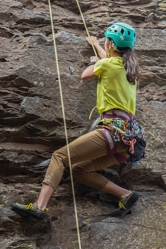 Woman wearing the Feathers Tech-T in Light Lime while rock climbing. Also wearing the Tobacco Colored Tinkham Pants. 