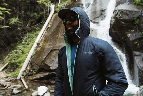 Man wearing Nightbreak Camo Ultra Lochi 2.0 in front of a waterfall with the hood up and unzipped