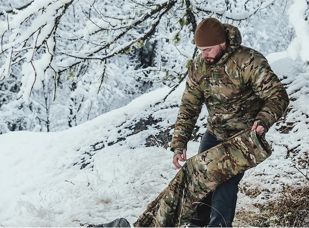 Man in camouflage clothing and hat standing in a snowy forest