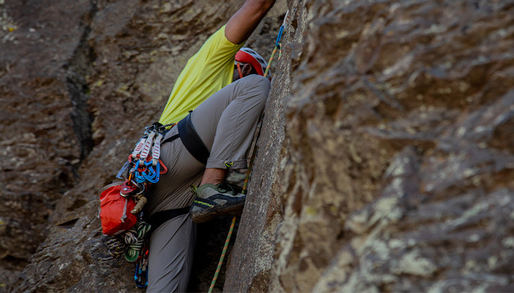 Rock Climber wearing the Tarn Good pants in Moonstone while on the side of a rock wall. Also wearing the SolarSwift Tech-T in the Light Lime color.