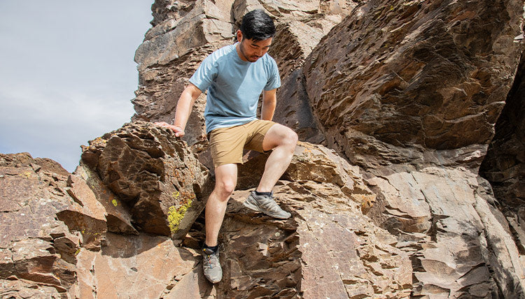 Man is descending a rocky slope wearing the SolarSwift Short Sleeve Shirt and the Tarngood Short in Tobacco color from Beyond Clothing.