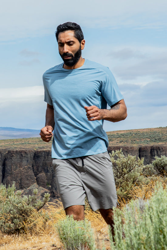 Man trail running through a high desert landscape wearing the Moonstone colored TarnGood Shorts and the Big Sky Blue SolarSwift Tech-T. 